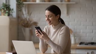 Young woman use cellphone sit at table in kitchen