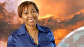 Beth A. Brown smiles at the camera there is a nebula scene in the background behind her.