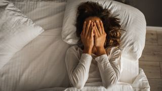 A woman in bed covering her face with her hands