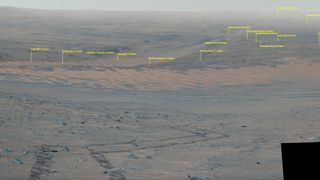 looking down the slope of a crater rim on mars, with rover tracks in the foreground. a dozen landmarks are identified via yellow text