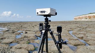 Several timelapse cameras attached to a tripod on a beach on a sunny day