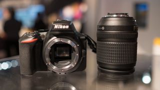 The Nikon D5600 next to a lens on a glass table