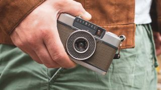 A hand holding a retro Olympus film camera