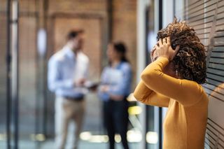 Stock image denoting sexism in the tech industry with female working holding her head and two colleagues in background.