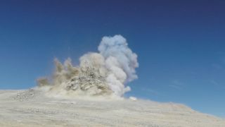 a large explosion causing material to rise up into the blue sky.