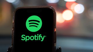 Spotify logo on phone, blurred city lights in background