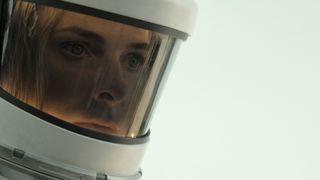 A woman's face seen through the visor of a hazmat suit