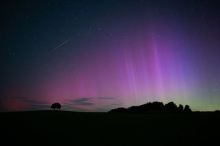 curtains of purple and blue light fill the sky with a long tail of a shooting star in the top left corner of the image.