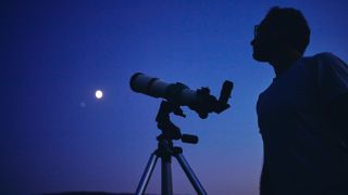 Telescopes at Walmart: Image shows man standing next to telescope looking at moon 