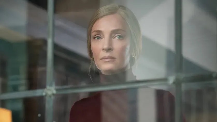 Uma Thurman looks out of a window and looks serious