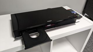 Panasonic DP-UB820 with disc tray open on white stand