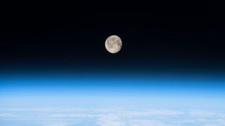 thin blue haze of earth&#039;s atmosphere with the moon shining above. 