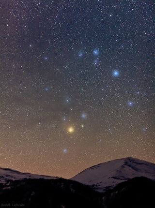 Antares, a red supergiant star in the constellation Scorpius, shines as the bright-red sparkle at the center of the image.