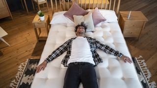 A man lies on top of a comfy white mattress placed on a supportive box spring