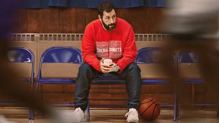 Adam Sandler as Stanley Beren sitting on a chair watching a basketball game with a basketball by his feet.