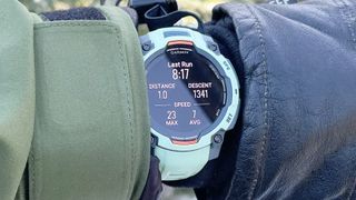 Garmin Instinct 3 on a user's wrist shown up-close in between a ski glove and jacket