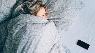 woman asleep with phone on bed next to her