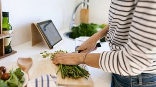 Woman preparing asparagus in kitchen while watching video on tablet