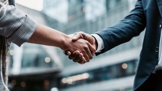 Two business persons shaking hands standing outside.