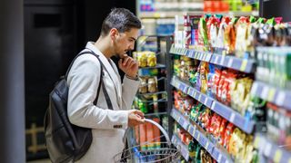 A man stands in the snack aisle of a grocery store looking at bags of chips