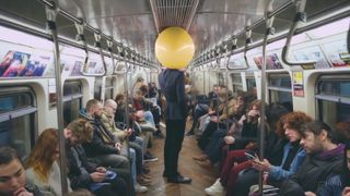 AI-generated image of a man in a dark suit with a yellow balloon head standing in a busy subway care