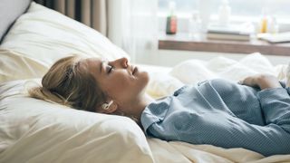 Woman lays on bed with her eyes closed and earbuds in her ears