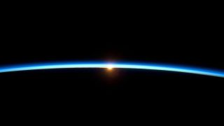 image of Earth&#039;s atmosphere appearing as thin blue line above Earth and the sun in the background 