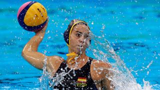 Beatriz Ortiz Munoz, in a black swimming costume and hat, rise from the water with the ball for Spain in the water polo at the 2024 Paris Olympic Games.