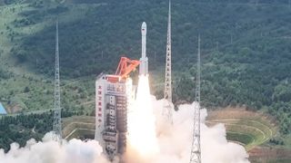 a white rocket launches with green hills in the background