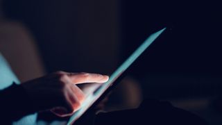 A woman's hand using a tablet, to represent women in tech. Decorative: the background is dark.