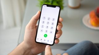 A hand holding a smartphone showing the phone number dialling screen