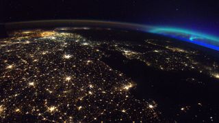 A photo of a blue aurora in the distance with city lights in the foreground