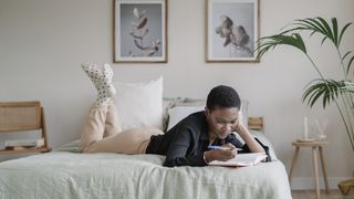 A woman lies on bed writing in her sleep diary