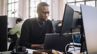 Software developer burnout concept image showing dev hunched over at a desk while working.