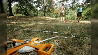 Here we see two people conducting an archaeological survey for a historic settlement in Central Park, New York. One person is using a ground-penetrating radar and the other is measuring out the site using a really long measuring tape.