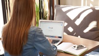 Woman with her back to the viewer, sitting at a table and using a laptop, with Google Search open