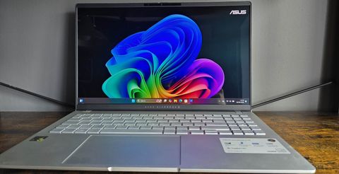 De Asus Vivobook S 15 Copilot+ in zilver op een houten bureau.