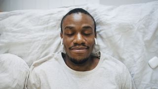 A man lies on his bed listening to a sleep podcast on his Apple AirPods