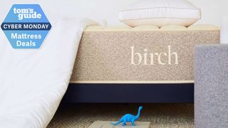 Birch Natural mattress closeup with a blue dinosaur toy at the bottom and a Tom's Guide Cyber Monday mattress deals badge in the top left