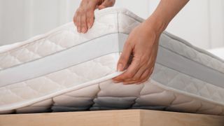 A person lifts up the edge of a mattress to rotate it