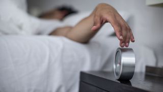 Man lying in bed and turning his alarm clock off