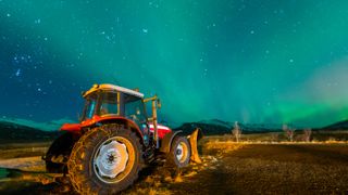 A red tractor in a field at night with blue auroras in the night sky