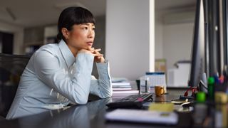 Female software engineer sitting idly at desk while staring at a desktop computer screen.