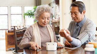 An elderly woman helps an elderly man check his blood pressure.