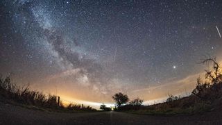 a timelapse photograph of the night sky showing several lyrid meteors streaking through the sky