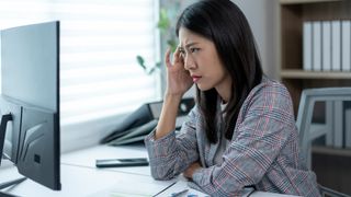 Vrouw zit aan een bureau en kijkt gefrustreerd naar een monitor