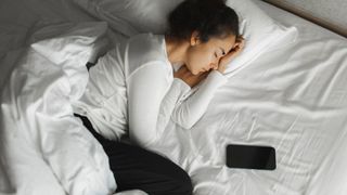 A woman sleeping on her side next to her smart phone