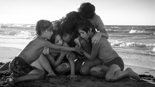 A black and white picture of the Roma cast hugging each other on the beach as the tide comes in behind them.