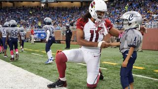 Arizona Cardinals football player shaking hands with a young fan on the pitch.