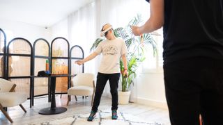 Hamish interacting with objects in VR while wearing a Meta Quest 3. They stand in front of a plant while someone watches on.